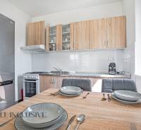 A kitchen in a 2-room apartment with a dining table, a stainless steel refrigerator, and a wooden kitchen unit.