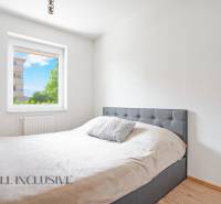 A bedroom in a 2-room apartment with a bed and a view of greenery through the window.