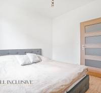 A bedroom in a two-room apartment with a bed and wooden doors, white interior.