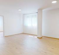 Spacious living room in a 2-room apartment with wooden flooring and white walls.