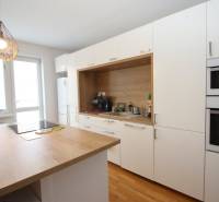 A kitchen in a 2-room apartment with built-in appliances, white cabinets, and wooden flooring.