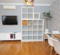A bright living room in a two-room apartment with a television and a shelving unit.