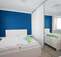 A bedroom in a 2-room apartment with a white bed and a large mirrored wardrobe.