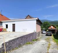 A family house in the village of Nitrica with a concrete yard and parked cars in front of the garage.