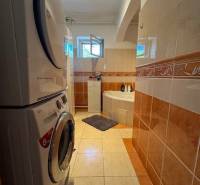 A bathroom in a family house with a washing machine, dryer, and bathtub, tiled with colorful tiles.
