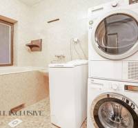 A bathroom in a family house with a window, a washing machine, and a dryer, cream tiles.