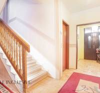 The interior of a family house with a wooden staircase, red carpets, and plants near the entrance.