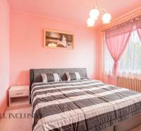 A bedroom with pink walls and curtains, a double bed, a painting, and a nightstand.