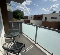 The balcony of a 2-room apartment in Stará Ľubovňa with furniture, a view of modern buildings and greenery.