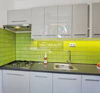 A kitchen in a studio apartment with a gas stove, green tiles, and a stainless steel sink.