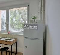 Dining area in a studio apartment with a refrigerator and a table by the window.