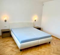 A bright bedroom with a double bed, wooden parquet floors, and two nightstands in a 2-room apartment.