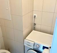 A bathroom with a washing machine in a 2-room apartment, tiled with light tiles.
