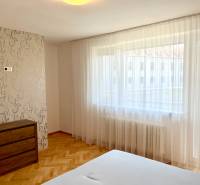 Bedroom in a 2-room apartment with large windows, wooden floor, and a dresser.