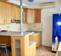 A kitchen in a studio apartment with light wooden furniture, a bar counter, and a blue refrigerator.