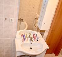 Bathroom in a studio apartment with a sink, bathtub, and mirror, beige tiles.