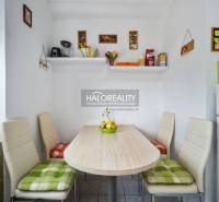 Dining room of a 2-room apartment with white chairs and shelves on the wall.