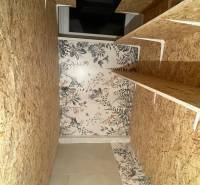 Storage space in a 3-room apartment with wooden shelves and floral wallpaper.