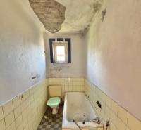 A worn-out bathroom in a family house with a damaged ceiling, bathtub, and toilet.