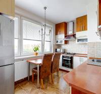 A kitchen in a 3-room apartment with a wooden cabinet, refrigerator, and dining table with chairs.