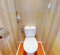 Toilet in a 3-room apartment with beige tiles and a toilet paper holder.