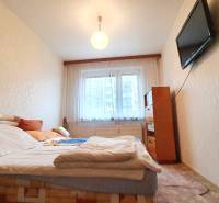 A bedroom in a three-room apartment with a TV on the wall and a bed.