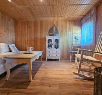 Interior of a cabin with a wooden floor, a swing, a table, and a display cabinet.