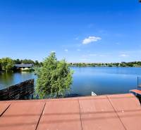 The view from the cottage in Čaňa to the lake with a blue sky and greenery.
