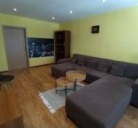 Living room with wooden flooring, gray sofa, chairs, and light yellow walls in a three-room apartment.