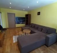 Living room with a large sofa, wooden floor, and a television in a 3-room apartment.