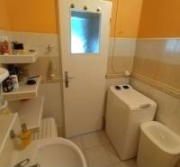A bathroom in a 3-room apartment with a sink, washing machine, and shelves for cosmetics.