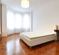A bright bedroom with large windows, a simple bed, and wooden flooring in a 3-room apartment.