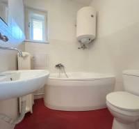 Bathroom with a corner bathtub, sink, toilet, and boiler in a 2-room apartment.