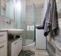 A bathroom in a studio apartment with a sink, shower, and washing machine.