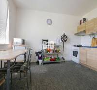A kitchen in a studio apartment with a dining table, appliances, and a chessboard on the wall.