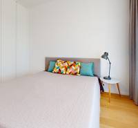 A bedroom in a 2-room apartment with a double bed, colorful pillows, and a nightstand.