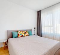 A bright bedroom with large windows, a bed, and colorful pillows in a two-room apartment.