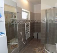 A bathroom in a family house with a corner shower and a shelf with towels.