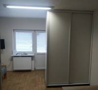 A studio apartment with wooden flooring, a wardrobe, and windows with blinds, ideal for living.