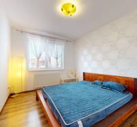 A bright bedroom with a wooden bed, blue blanket, and wallpapered wall in a four-room apartment.