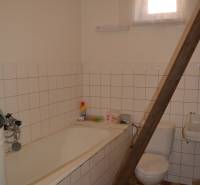 A bathroom with a bathtub and a toilet in a family house, with tiles and wooden stairs.