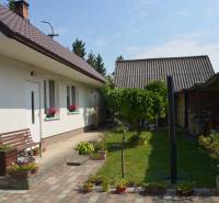 A family house in Trstín with a landscaped garden, a bench, and plant details.