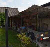 The courtyard of a family house in Trstín with a shelter, a trailer, and plants in pots.