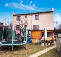 A two-story family house with a trampoline in the garden, a greenhouse, and outdoor seating.