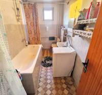 A bathroom with a shower, washing machine, sink, and patterned floor in a family house.