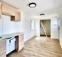 A kitchen in a cabin with a wooden floor, white walls, and a ladder to the upper floor.