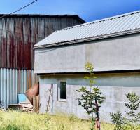 A cottage in Cífer surrounded by greenery, next to a metal structure, with a lawn in the foreground.