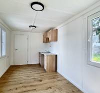 A simple interior with wooden flooring, windows, and a kitchen unit in a cottage.