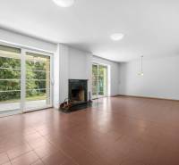 A spacious living room in a villa with a fireplace, large windows, and tiled flooring.