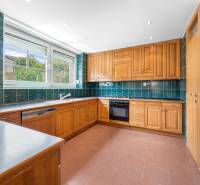 A kitchen in a villa with wooden cabinets, green tiles, and a large window.